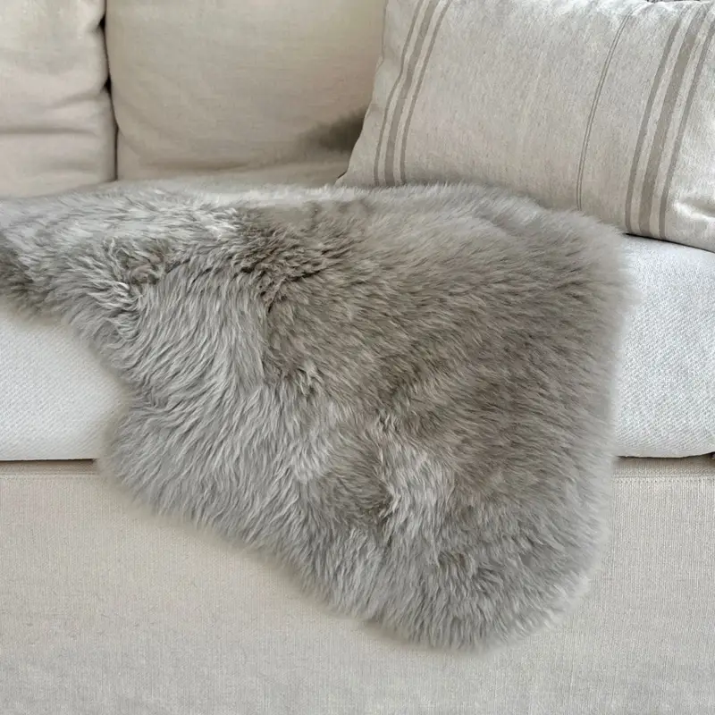 Pebble coloured sheepskin rug on a cream sofa with cream cushions.