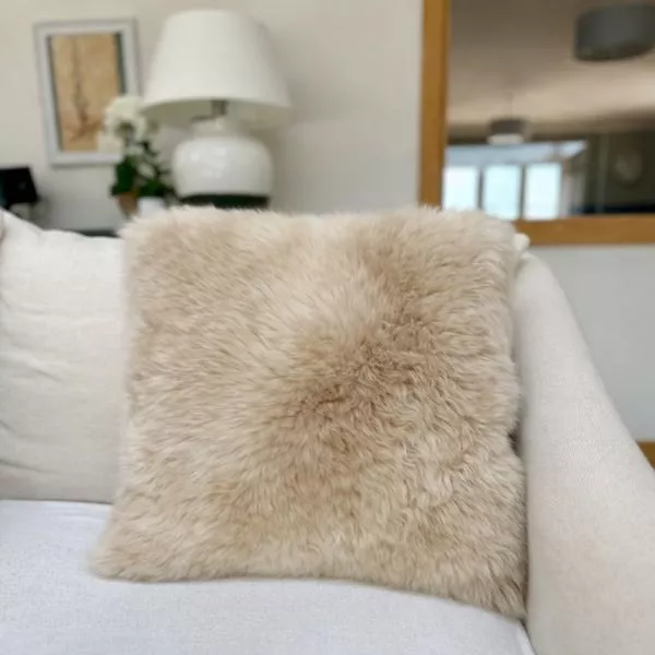 An square sheepskin cushion in eggshell colour on a cream sofa in a bright, modern, cosy room.