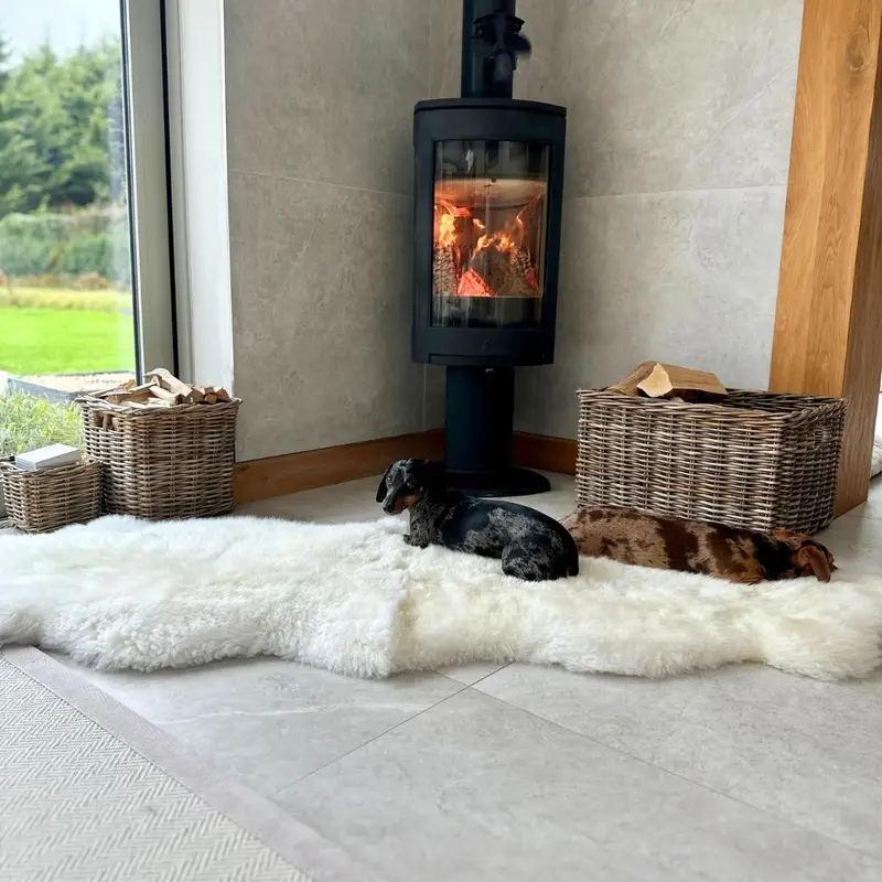 A double sheepskin rug in ivory in front of a fire.