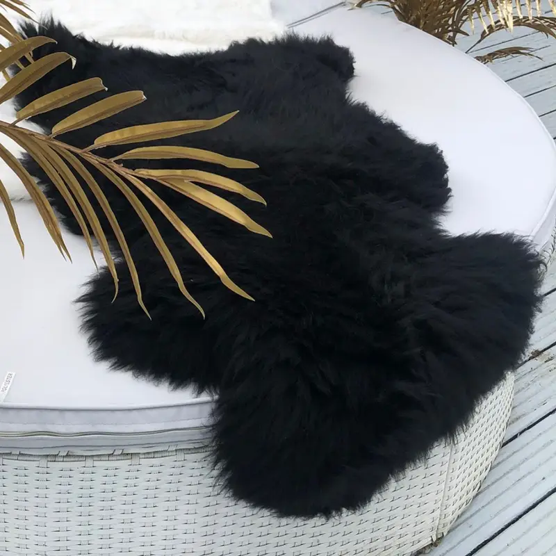 Coal Black sheepskin rug on a white sofa with gold coloured planting.