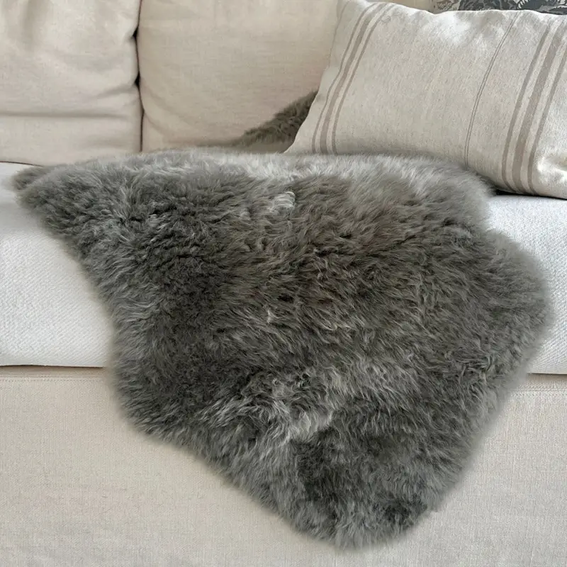 Fossil grey sheepskin rug close up of texture on a cream sofa.