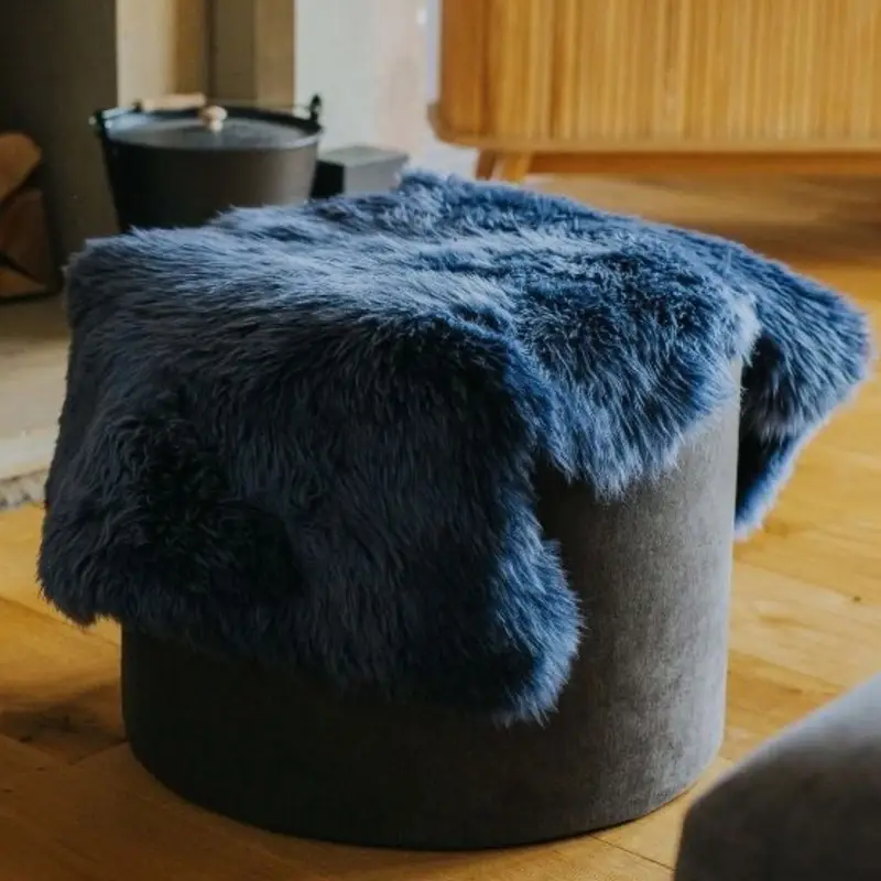 A navy blue sheepskin rug draped over a pouffe in front of a fire.