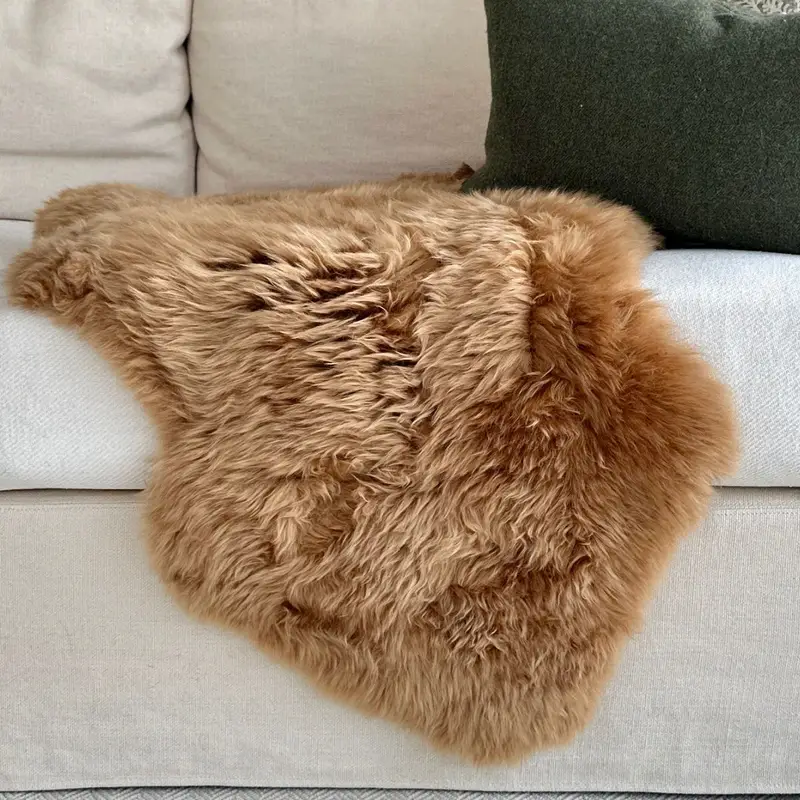 A close up of a Pumpkin spice sheepskin rug draped on a cream sofa.