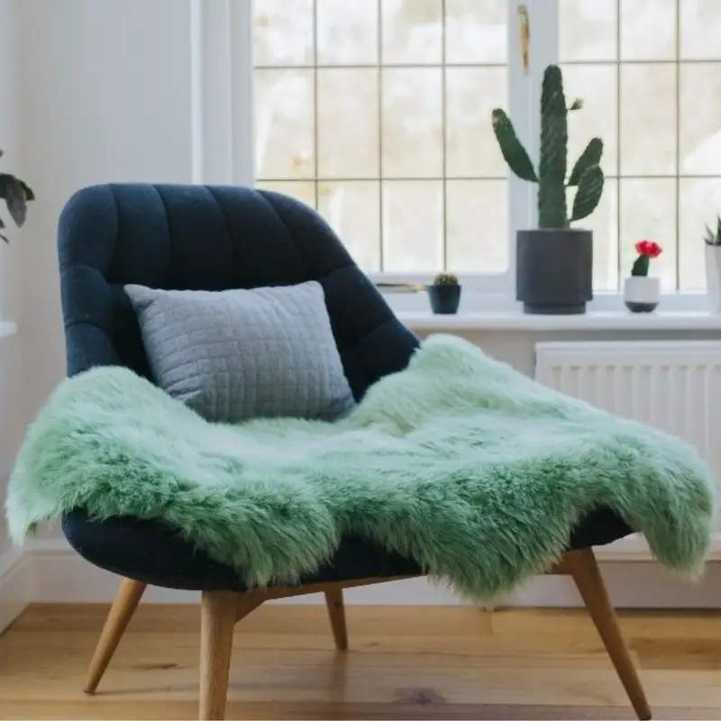 Sage green coloured sheepskin rug on a chair next to a bright window.