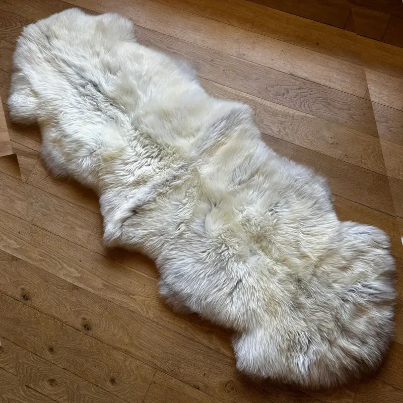 Pretty ivory and grey rare breed sheepskin rug on a wooden floor in natural daylight