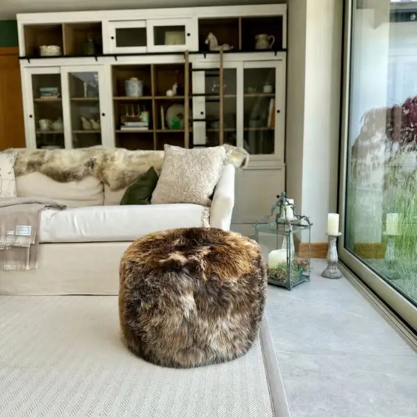 An extra large sheepskin pouffe in burnt caramel and nutty tones with vanilla flecks in a modern room in front of a cream sofa.