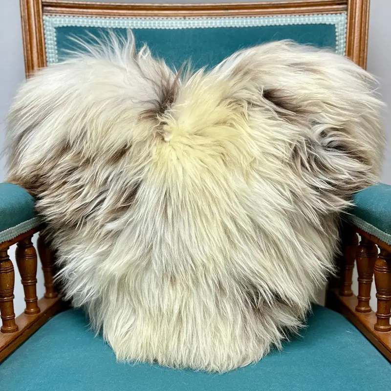 British rare breed heart shaped sheepskin cushion styled on a blue velvet chair, showing natural wool texture and depth.