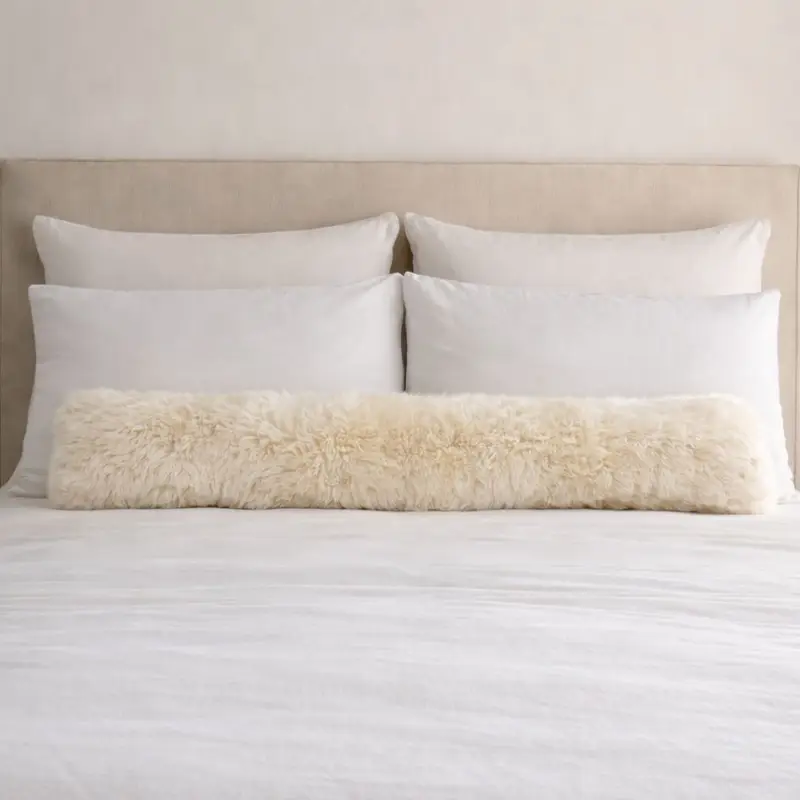Long sheepskin bolster cushion layered on a bed in a soft neutral bedroom