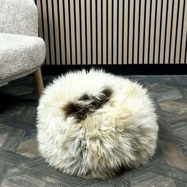 A natural rare breed sheepskin cushion on a wooden floor next to a sheepskin chair.