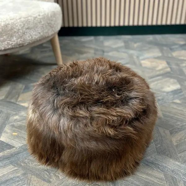 Reverse of a lovely soft textured natural chocolate rare breed sheepskin pouffe on a wooden floor next to a sheepskin chair.