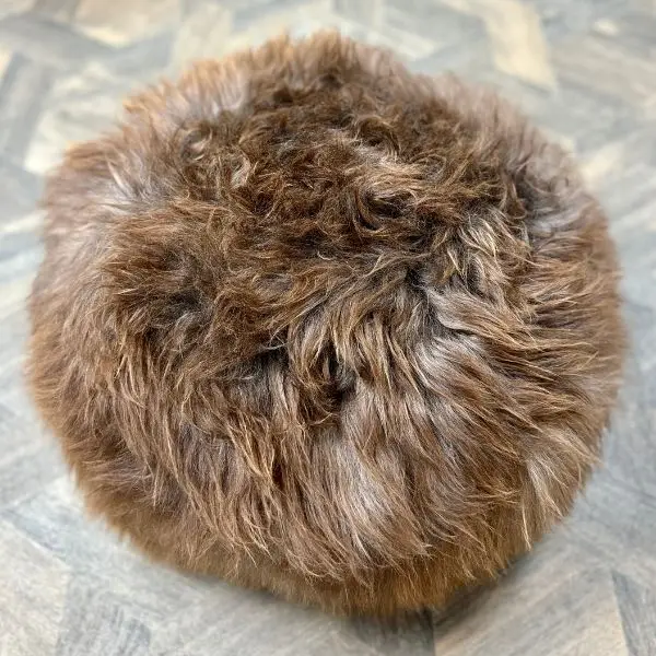 Top of a lovely soft textured natural chocolate rare breed sheepskin pouffe on a wooden floor next to a sheepskin chair.