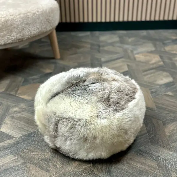 Reverse of a lovely velvet textured natural grey rare breed sheepskin pouffe on a wooden floor next to a sheepskin chair.