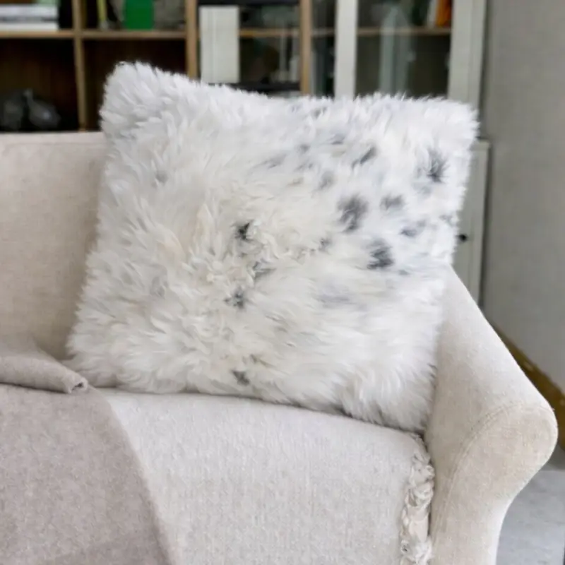 Natural rare breed sheepskin cushion resting on a cream sofa with gentle daylight.