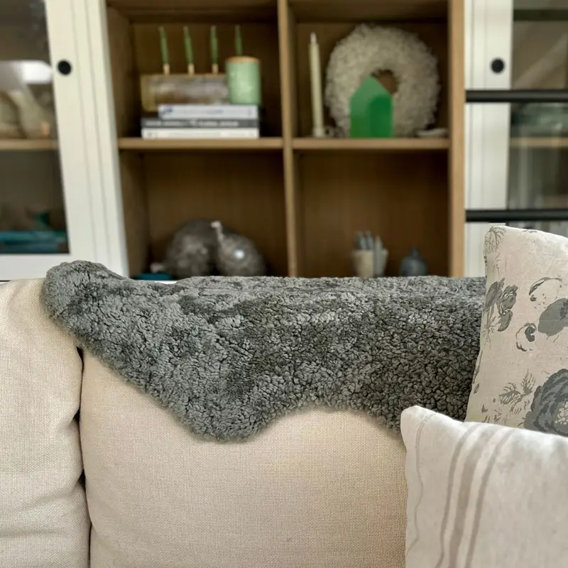 Fossil boucle sheepskin (short curly) on a cream sofa with cushions and bookshelves behind