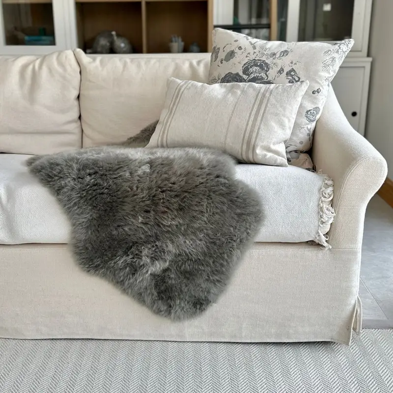 Fossil coloured sheepskin throw on a cream sofa with cushions, styled in front of bookshelves