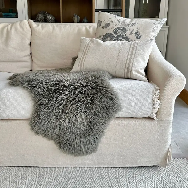 Fossil yeti sheepskin (long wool curly) draped over a cream sofa with cushions, bookshelves behind