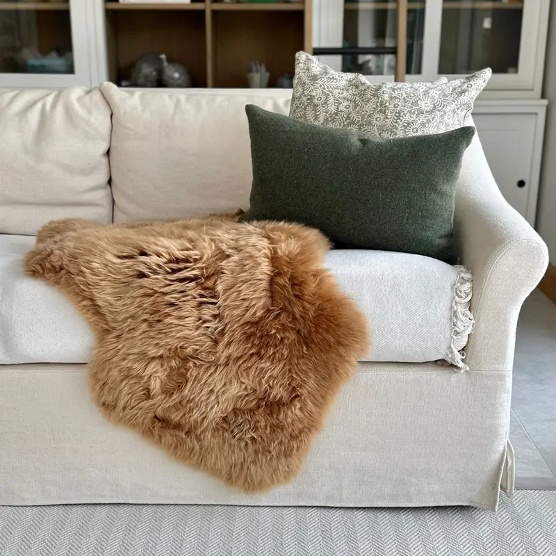 Pumpkin spice sheepskin draped on a cream sofa with cushions, styled in front of bookshelves