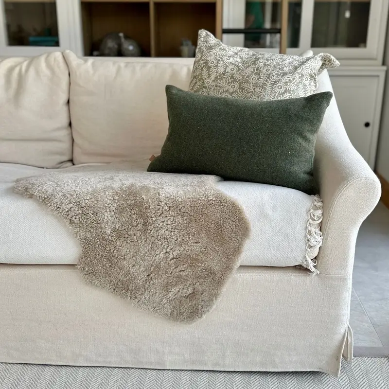 Eggshell boucle sheepskin (short curly) draped on a cream sofa with cushions, bookshelf styling