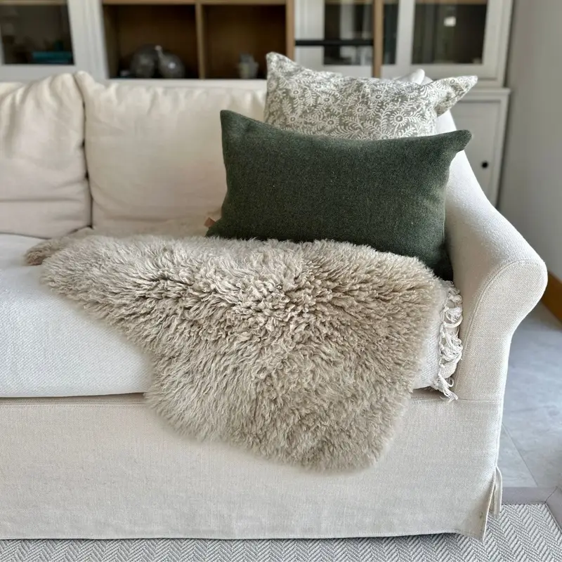 Eggshell yeti sheepskin (long wool curly) on a cream sofa with cushions, bookshelves behind