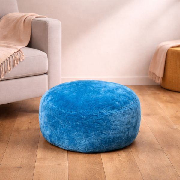 Velvety sheepskin pouffe in a vibrant aqua colour in a neutral room next to a cream sofa.