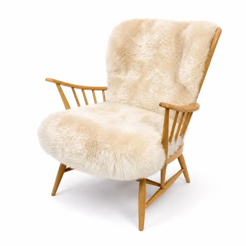 Angle view of vintage Ercol chair with curved wooden frame and sheepskin cushions