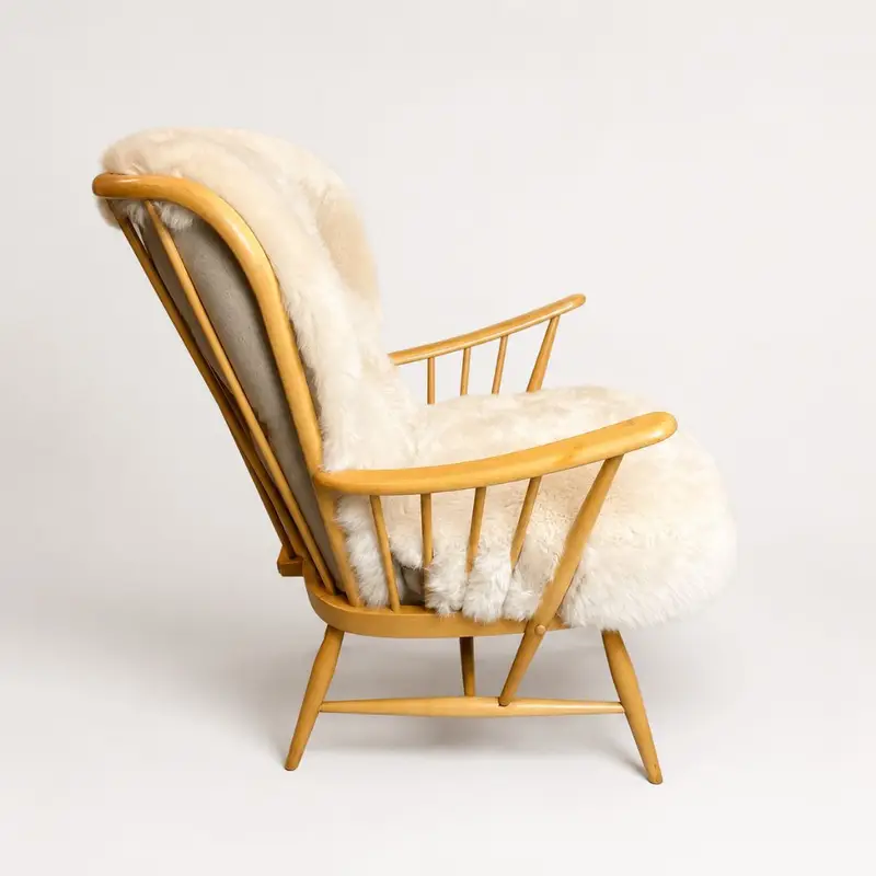 Side view of vintage Ercol chair with curved wooden frame and sheepskin cushions