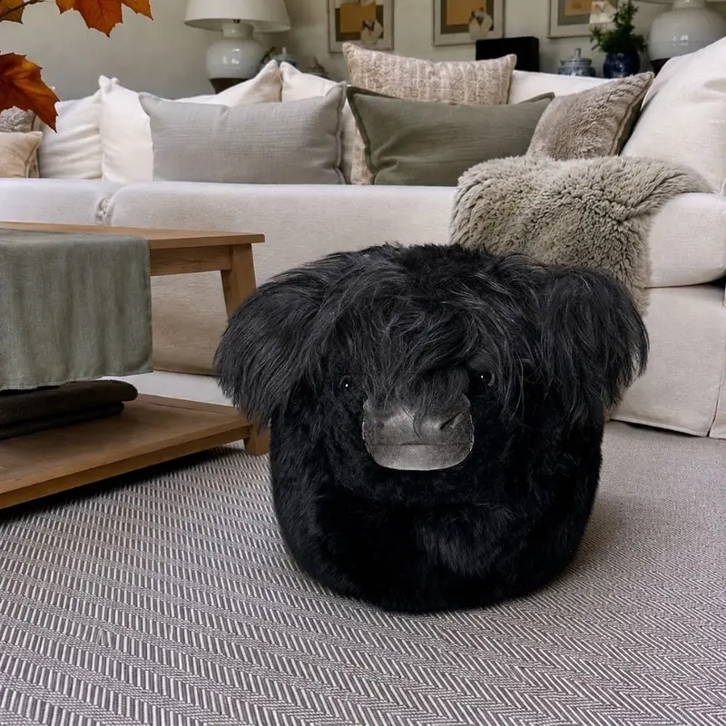 Large Welsh Black cow pouffe handmade from long black sheepskin with shaggy ears in a neutral living room